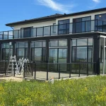 Black-framed glass enclosure at the back of a modern home with a balcony above