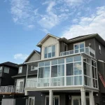 Grey home with a glass-enclosed upper balcony and a lower deck