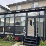 Black-framed glass enclosure with steps at the back of a house
