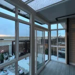 Corner of a glass enclosure with white-framed windows and a clear roof
