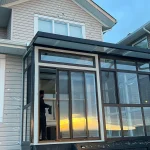 Dark-framed glass sunroom with sliding doors reflecting a sunset