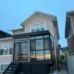 Black-framed glass sunroom with steps at the back of a house