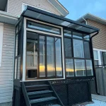 Black-framed glass sunroom with steps at the rear of a house