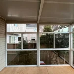 Inside a glass patio enclosure with white-framed windows and a wood deck floor