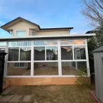 White-framed glass patio enclosure on a wooden deck behind a house