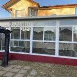 White-framed glass patio enclosure beside a gazebo and paving stones