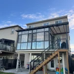 Home with an upper-level glass enclosure, outdoor stairs and a play area below